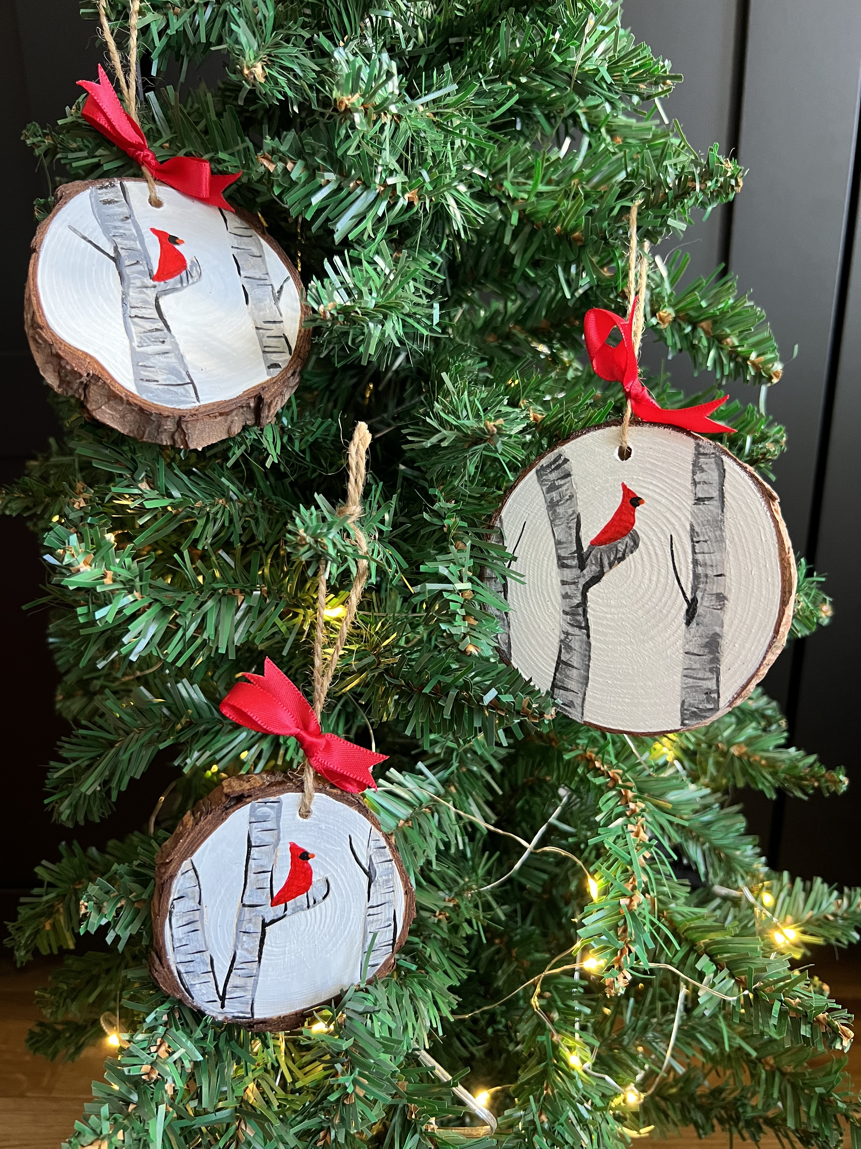 three hand painted wooden slices, painted with birch trees and one cardinal. String attached to turn them into Christmas ornaments.