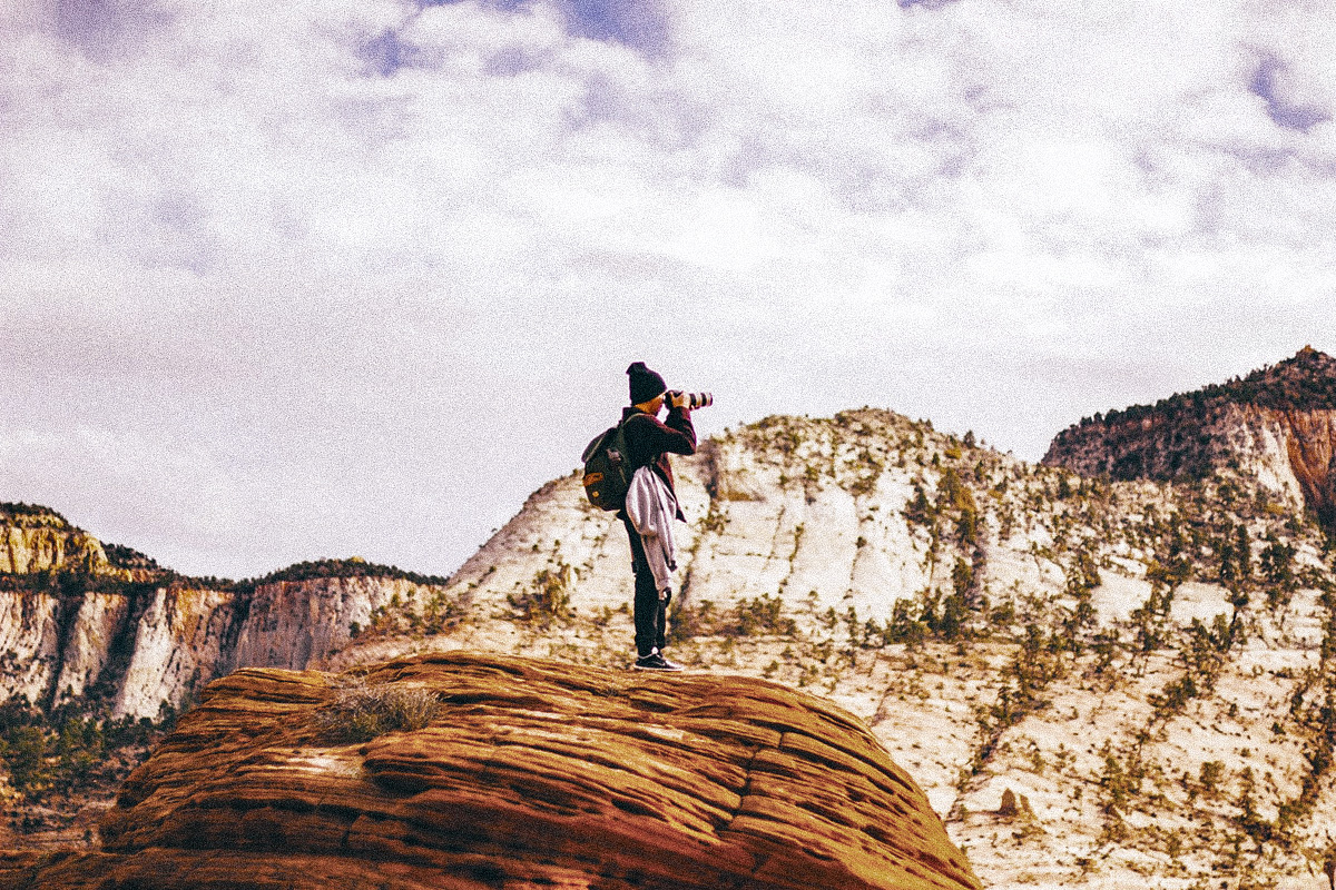 Person standing on a rock taking photos of a mountainous landscape with a camera.